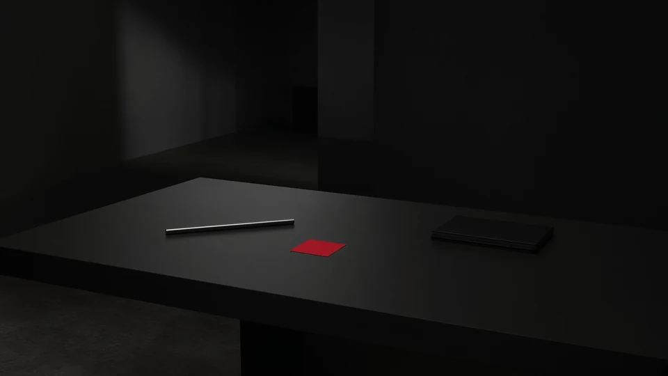 A dark tabletop with a slim metal object, a red card, and a black device